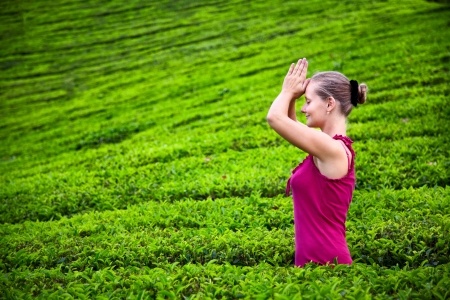 Praying woman with hands in namaste in red cloth on tea plantations in Munnar hills, Kerala, India